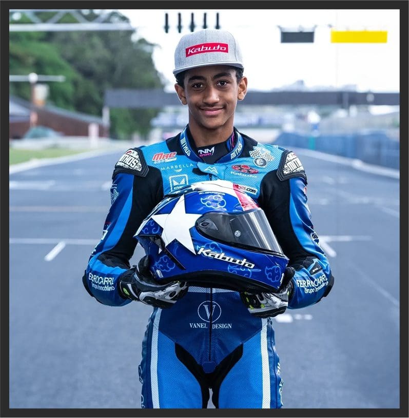 A man in blue racing suit holding a helmet.